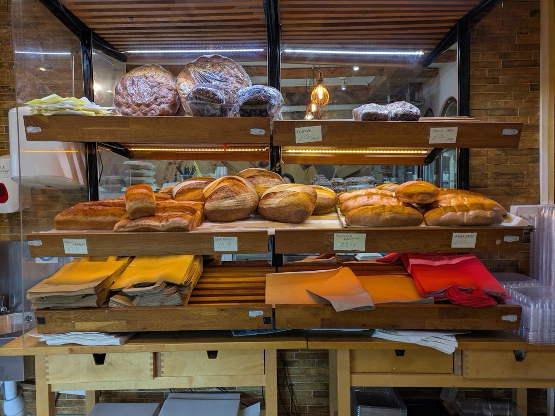 A wooden shelf of freshly baked bread including sourdough loaves, batons and cozonac