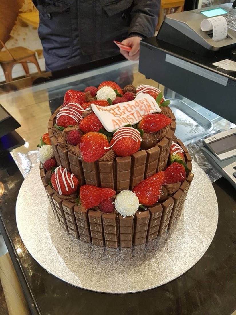 A two-tier chocolate celebration cake edged with chocolate fingers and topped with fresh strawberries